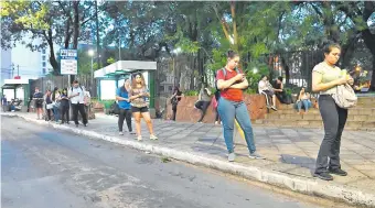  ?? ?? Pasajeros apostados en una parada sobre la avenida Mariscal López, frente a la plaza Infante Rivarola del barrio Villa Morra, observan sus celulares para sobrelleva­r la larga espera.