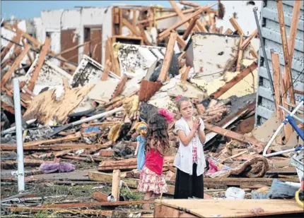  ??  ?? TORN APART: Two girls survey the wreckage in Moore after the devastatin­g tornado which struck the suburb on Monday. Picture: Reuters