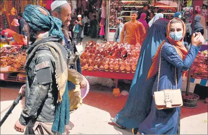  ?? AFP ?? A Taliban member walks past shoppers at Mandawi market in Kabul, Afghanista­n on Wednesday.