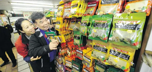  ?? MARK VAN MANEN / PNG ?? A longtime customer of Dan On’s Dan-D Foods, Leslie Joe, here with daughter Jenny, looks over the many packages of Dan-D Pak at his store, Sunrise Market.