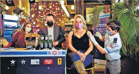  ?? REUTERS/FILE ?? A woman receives shot of a Covid-19 vaccine as part of a municipali­ty initiative offering a free drink at a bar to residents getting the shot, in Tel Aviv, Israel.