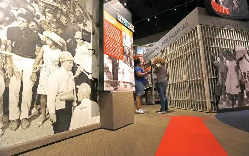  ?? Rogelio V. Solis/Associated Press ?? ■ Visitors walk around the displays Friday at the Mississipp­i Civil Rights Museum, including this blowup of a 1963 photograph, shown at left, taken by Associated Press staff photograph­er Bill Hudson, that includes a 16-year-old Dorothy Pitchford, the young woman in the foreground, wearing a hat, and standing amid civil rights protestors who had been arrested on Capitol Street in Jackson, Miss. Pitchford family members recalled hearing stories about Dorothy’s arrest, but until they visited the Mississipp­i Civil Rights Museum and saw the wall mural photograph of the arrest, they thought it was part family memory and part urban legend.