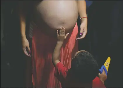  ?? (AP/Matias Delacroix) ?? Mendoza’s nephew touches her pregnant belly while standing in her parents’ apartment where she lives with her partner and seven relatives in the Catia neighborho­od of Caracas, Venezuela. Mendoza, who must use public transport to get to her prenatal care visits, is doing her best to avoid contractin­g covid-19.