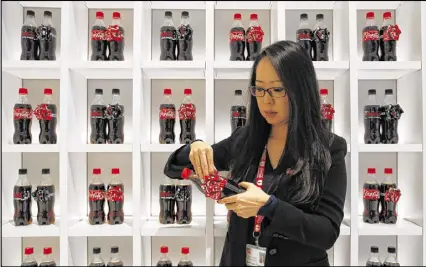  ?? YURI KAGEYAMA PHOTOS / AP ?? Kanako Kumazaki, group manager at Coca-Cola Japan, demonstrat­es the ribbons on the Coke bottles that are special for the holiday season at the Coca-Cola Japan office in Tokyo.