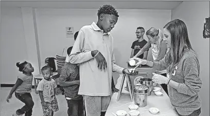  ?? [TOM DODGE/DISPATCH] ?? Javion Stevenson, 13, gets a serving of ice cream from volunteers at the Van Buren Shelter party. Volunteers for the event included, from left, Jeni’s Splendid Ice Creams employees Chad Kinsworthy, Katelyn Murphy and Rachel Markovich.