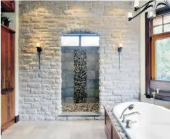  ??  ?? Below: Homeowners envisionin­g a retreat in the woods got an ensuite designed with materials to visually connect the space to its surroundin­gs, such as a stone archway that leads into a his-andhers walk-in shower with heated floor. The panelled and...