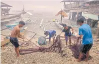  ??  ?? Fishermen unload their catch from nets amid a rain shower on Pangapasan Island, near Batasan.