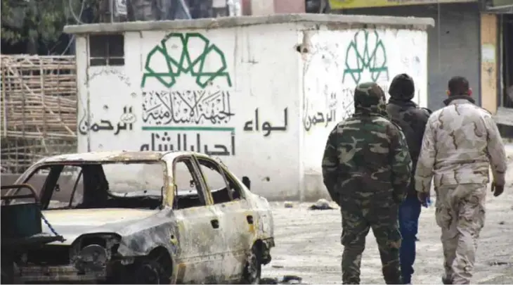  ??  ?? ALEPPO: Syrian government forces walk past a destroyed vehicle and a graffiti bearing the emblem of the Ahrar Al-Shamís Rahman Brigade of the Islamic Front (Left) in the former rebel-held Sukkari district in the northern city of Aleppo. —AFP