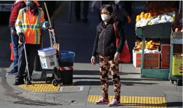  ?? Associated Press ?? ■ A masked worker and shopper wait for a street signal Friday in the Chinatown district in San Francisco. As China grapples with the growing coronaviru­s outbreak, Chinese people in California are encounteri­ng a cultural disconnect as they brace for a possible spread of the virus in their adopted homeland.