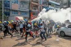  ?? Associated Press ?? Anti-coup protesters run as one of them discharges a fire extinguish­er to counter the impact of tear gas fired by riot policemen Wednesday in Yangon, Myanmar.