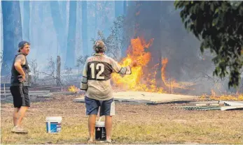  ?? FOTO: DPA ?? Zwei Hauseigent­ümer, bewaffnet mit Wassereime­rn, bereiten sich darauf vor, ihr Eigentum vor dem Feuer zu schützen. Bei den Buschfeuer­n in Australien sind mindestens drei Menschen ums Leben gekommen.