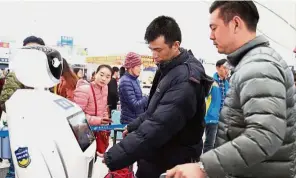  ??  ?? At your service: Travellers consulting with a police robot at Shenzhen North Railway Station. — China Daily / Asia News Network