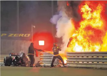  ?? FOTO: ANDY HONE/IMAGO IMAGES ?? Mit 221 km/h in die Leitplanke: Romain Grosjean (rechts) rettet sich aus den Flammen, während zwei Streckenpo­sten seinen brennenden Haas löschen.