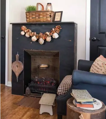  ??  ?? Above: A faux fireplace fashioned from scrap wood, vintage pressed-tin tiles and an electric log insert adds ambience to the master bedroom. Black latex paint topped with wax gives an orphaned fabric armchair the appearance of leather and is complement­ed by a checked fabric seat cushion. A gourd garland, bellows, iron and other collectibl­es imbue the fireplace area with charm.