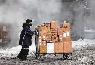  ?? Angus Mordant / Bloomberg ?? A driver for an independen­t contractor to FedEx Corp. pushes a cart of packages through snow in New York City last week.
