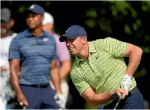  ?? AP ?? First-round leader Rory McIlroy closely follows his tee shot on the 17th hole as playing partner Tiger Woods looks on in the background.