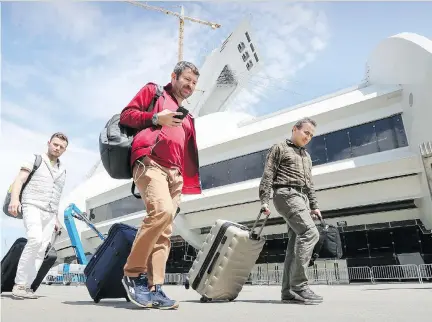  ?? JOHN MAHONEY ?? From left, Turkish refugees Cagatay Karaman, Ibrahim Yurtseven and Muhsin Yanik drag their suitcases as they leave the temporary refugee centre at the Olympic Stadium in Montreal on Monday, after no longer being able to tolerate the living conditions.