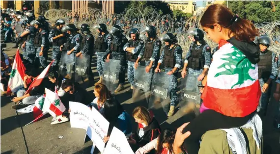  ?? Reuters ?? A girl wears the national flag draped over her body as riot police stand guard during the ongoing anti-government protest in Beirut. Hezbollah supporters spread rumors to hijack the people’s movement.