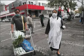  ?? (AP/Dolores Ochoa) ?? A nun wears a face mask and disposable gloves Saturday as she walks with a worker carting her groceries to a waiting taxi in Quito, Ecuador.