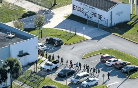  ??  ?? Students are evacuated Wednesday by police from Marjory Stoneman Douglas High School in Parkland, Fla., after a shooter opened fire on the campus, killing at least 17.