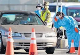  ?? AMY BETH BENNETT/SOUTH FLORIDA SUN SENTINEL ?? A woman cups her ear to hear while keeping her distance from a patient being screened at the COVID-19 drive-thru testing site at the Hard Rock Stadium in Miami Gardens.