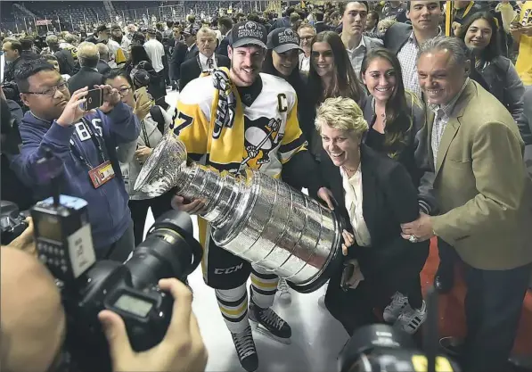  ?? Matt Freed/Post-Gazette ?? Sidney Crosby always seems to be the center of the attention, like Sunday night when photograph­ers and members of the Lemieux family surround him as he carries the Stanley Cup after the Penguins defeated the Nashville Predators, 2-0, for their second consecutiv­e title.