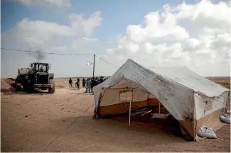  ?? PHOTO: AP ?? Palestinia­ns watch as a bulldozer raises protective sand berms around the tents at the Gaza Strip’s border with Israel.