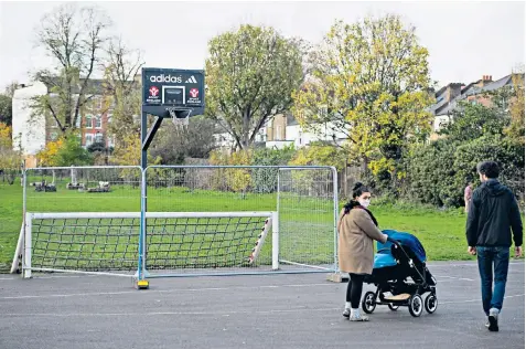  ??  ?? A family walks past barriers placed in front of a goal and basketball net at Warwick Gardens in Peckham, London, to stop people using them