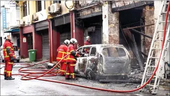  ?? ?? Firefighte­rs dousing the burnt car next to one of the shophouses, affected by the fire that struck Jalan Ewe Hai on Friday. — Photo by Chimon Upon