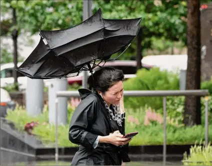  ?? Mark Lennihan / Associated Press ?? A woman’s umbrella is flipped inside out as she walks on a rainy and windy New York street on Friday. Fast-moving Tropical Storm Elsa hit the New York City region with torrential rains and high winds.