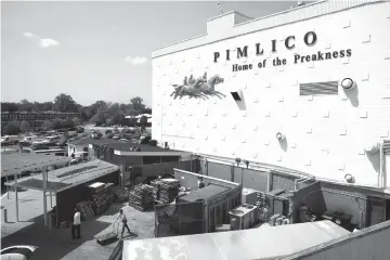  ?? Patrick Semansky/Associated Press ?? ■ People walk outside of a building at Pimlico Race Course on Tuesday as preparatio­ns take place for the Preakness Stakes horse race in Baltimore. Pimlico Race Course is getting all gussied up again this week, ready to host the Preakness on a day that...