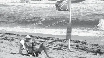  ?? PHOTOS BY JOE CAVARETTA/SOUTH FLORIDA SUN SENTINEL ?? Richard Desmoni of Boca Raton rests near a red flag warning people of severe hazards at Red Reef Park.