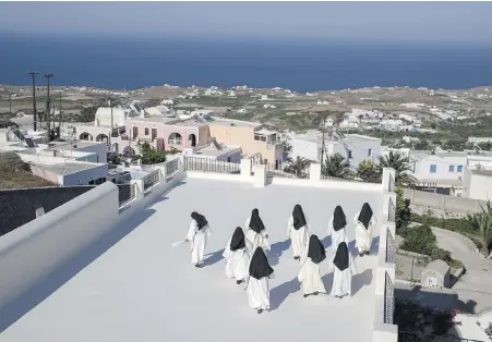  ?? PETROS GIANNAKOUR­IS, THE ASSOCIATED PRESS ?? Cloistered nuns walk on a terrace of the Catholic Monastery of St. Catherine on the Greek island of Santorini. Twice a day, the nuns recess to chat on the convent’s wide terraces, the Aegean Sea shimmering in the distance.