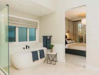  ??  ?? The freestandi­ng soaker bath hosts black faucets amidst white subway wall tile. Beyond, the master bedroom features a coffered ceiling with crown mouldings and wainscotin­g.