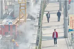  ??  ?? Men walk by a constructi­on site, separated by a wall installed with water misting system for dust control, in Shanghai, China. – Reuters photo