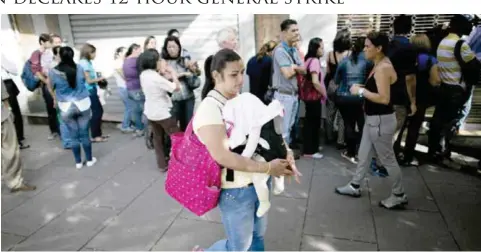  ?? AP ?? CARACAS: A woman carries her baby past a line of people waiting to buy products at a pharmacy in Caracas, Venezuela yesterday. —