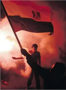  ?? AHMED GOMAA/THE ASSOCIATED PRESS ?? Secular Egyptian activists wave the flag as flares light up Wednesday in a Cairo protest against a new law regulating demonstrat­ions.