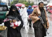  ?? EBRAHIM NOROOZI / AP ?? An Afghan woman walks through the old market as a Taliban fighter stands guard, in downtown Kabul, Afghanista­n, on Tuesday.