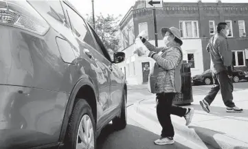  ?? ANTONIO PEREZ/CHICAGO TRIBUNE PHOTOS ?? Street vendor Carmen Nava brings an order of tamales to a customer’s car in 4300 block of West Armitage Avenue in Chicago’s Hermosa neighborho­od on June 19. At right is her husband Luis Melendez.