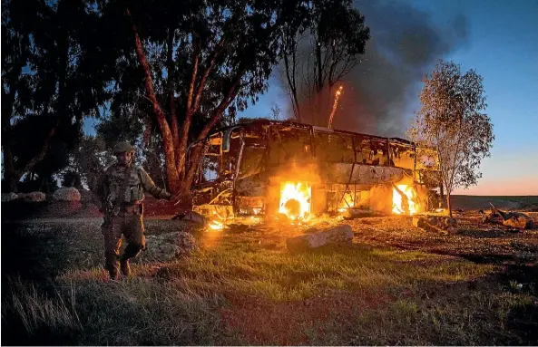  ?? AP ?? An Israeli soldier stands near a burning bus after it was hit by a mortar shell fired from Gaza. Israel’s military says it is prepared to step up its efforts against Palestinia­n militants in the Gaza Strip if rocket fire at Israel continues.