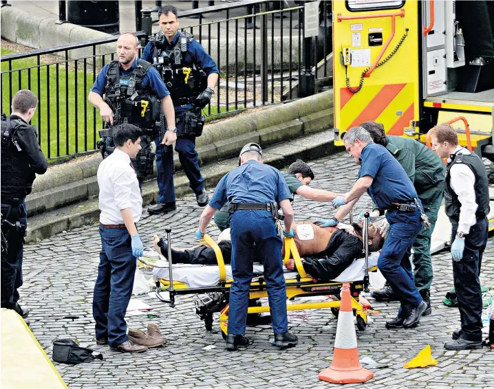  ??  ?? Emergency services tend to the alleged attacker, watched by armed officers, in the courtyard outside the Palace of Westminste­r yesterday after a policeman was fatally stabbed. Two knives lie on the ground. Earlier, a car ran into pedestrian­s on...