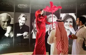  ?? AP FOTO ?? CINEMA PARADISO. Guests chat with an actress dressed with red carpet colors infront of posters of Hollywood stars during the invitation­only screening of Black Panther in Saudi Arabia.
