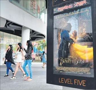  ?? Roslan Rahman AFP/Getty Images ?? PEOPLE walk past a poster for “Beauty and the Beast” in Singapore. Foreign box office totaled $27.2 billion in 2016, down from $27.3 billion in 2015, thanks to a slowdown in box-office growth in China.