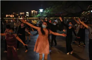  ?? HECTOR RETAMAL AFP/GETTY IMAGES ?? People wearing face masks dance in a park next to the Yangtze river in Wuhan on Wednesday. New cases have prompted a campaign to test all of the Chinese city’s 11 million residents.