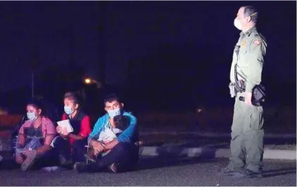  ?? AP PHOTO/JULIO CORTEZ ?? A migrant man, second from right, holds a child as he looks at a U.S. Customs and Border Protection agent at an intake area after crossing the U.S.-Mexico border in March in Roma, Texas. The Biden administra­tion said Monday that four families separated at the Mexico border during Donald Trump’s presidency will be reunited in the United States this week in what Homeland Security Secretary Alejandro Mayorkas calls “just the beginning” of a broader effort.