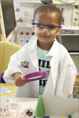  ?? Brodie Johnson • Times-Herald ?? Two-year-old Lafayette Malone Jr., is all decked out in his white coat and protective glasses as he uses a magnifying glass to inspect the plastic insects in a box on the table at a local daycare.