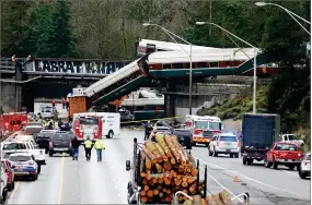 ?? AP PHOTO BY ELAINE THOMPSON ?? Logging trucks remain stopped just before where cars from an Amtrak train lay spilled onto Interstate 5 below alongside smashed vehicles as some train cars remain on the tracks above Monday in Dupont, Wash.