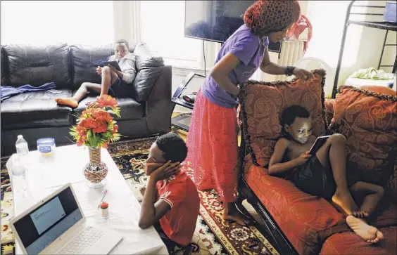  ?? Photos by Paul Buckowski / Albany Times Union ?? Bisoci Mnyomoelwa, second from right, a senior at Albany High School, sets her brother, Asukulu Oredi, up on the couch for his remote classroom time at their home in Albany. Bisoci's other brothers, Mmunga Oredi, background, and Mlondani Mnyomoelwa work remotely at the same time.