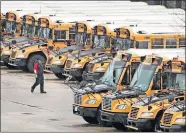  ?? ASSOCIATED PRESS] ?? A worker passes public school buses parked at a depot, Monday, in Manchester, N.H. [CHARLES KRUPA/ THE