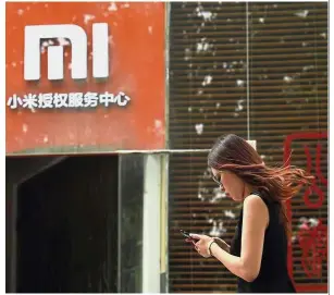  ??  ?? Soaring shipments: A file picture showing a woman walking past a Xiaomi service centre in Beijing. The company’s smartphone shipments jumped 88% from the same quarter a year earlier. — AFP